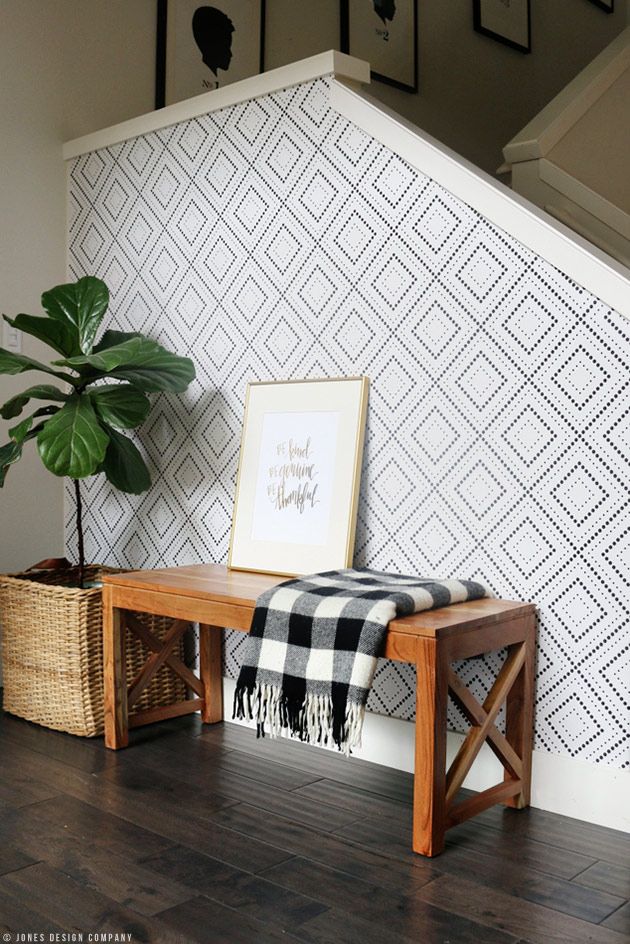 a wooden bench sitting in front of a wall with a potted plant on top of it