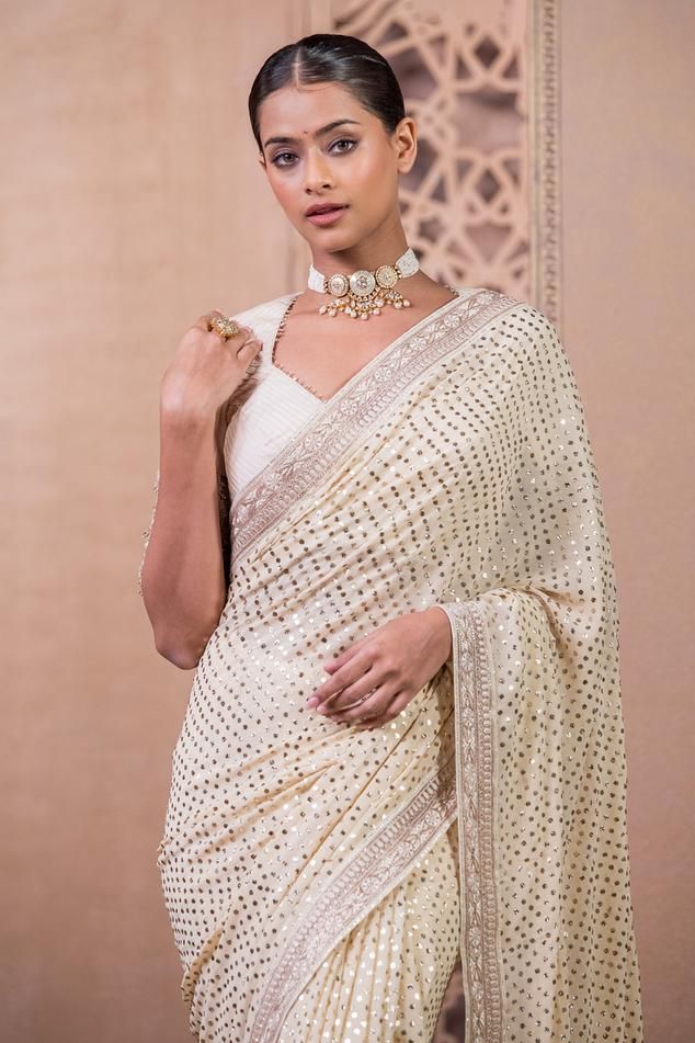 Ivory, gold georgette saree is uplifted with mukaish work and accentuated with a hand-embroidered border. Paired with a textured blouse in chanderi with embroidered sleeves.
Components: 2
Pattern: Embroidered
Type Of Work: Mukaish
Neckline: Sweetheart
Sleeve Type: Half
Fabric: Saree : Georgette, Blouse : Chanderi
Color: Ivory,Gold
Other Details: 
Tassel sleeves
Back cutout
Occasion: Wedding,Bride - Aza Fashions Elegant White Pre-draped Saree With Pallu, Festive Cream Georgette Pre-draped Saree, White Pre-draped Saree With Gota Work For Navratri, Elegant Gold Blouse Piece With Mirror Work, Gold Georgette Blouse Piece With Mirror Work, Gold Anarkali Georgette Blouse, Elegant Georgette Saree With Gota Work, Bollywood Style Cream Pre-draped Saree With Zari Work, Elegant White Chinon Pre-draped Saree