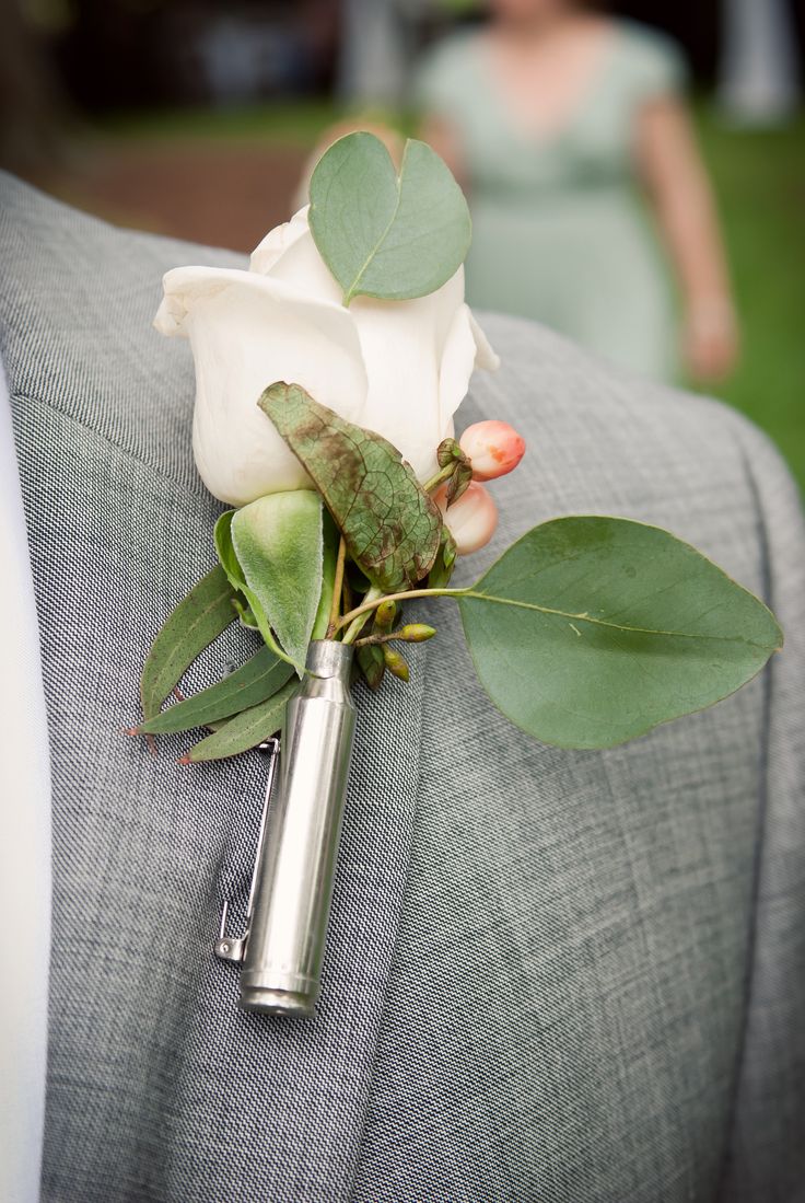 a boutonniere with a white rose and green leaves on the lapel