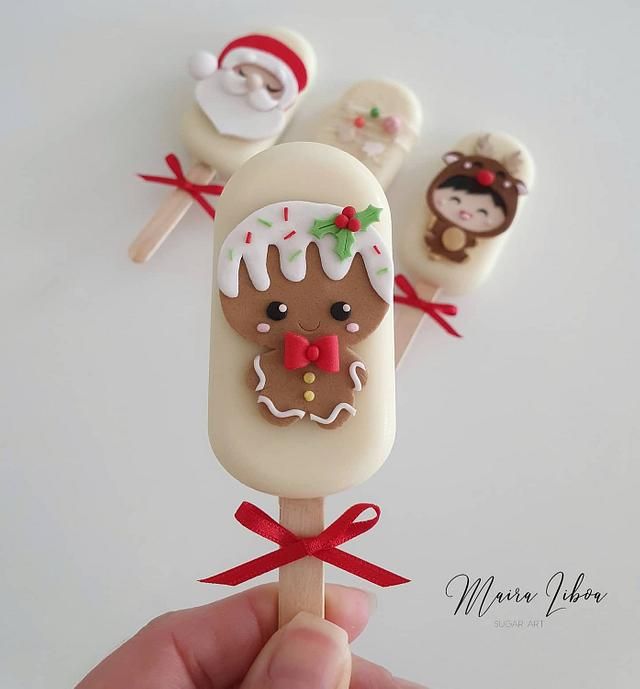 a hand holding a popsicle decorated with frosting and christmas decorations on top of it