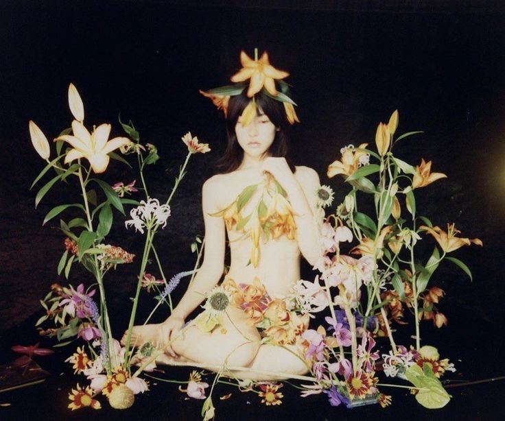 a woman sitting in the middle of flowers with her body surrounded by leaves and flowers