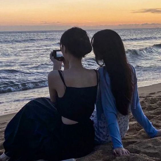 two women sitting on the beach looking at the ocean