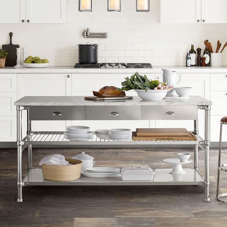 a stainless steel kitchen island with plates and bowls on it in front of white cabinets