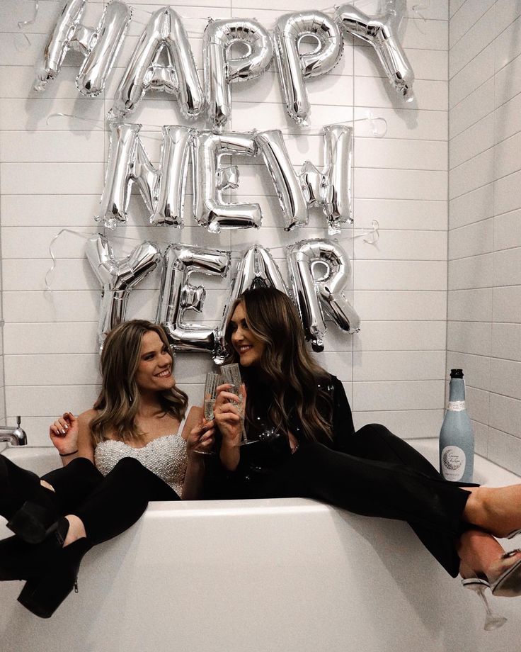 two women sitting on a bathtub with champagne in their hands and the words happy new year above them