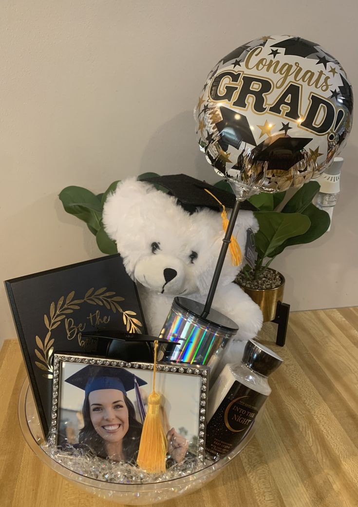 a white teddy bear sitting in a graduation gift basket with balloons and confetti