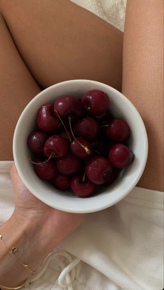 a woman holding a white bowl filled with cherries