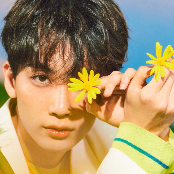 a young man holding two yellow flowers to his face while wearing a white shirt and green sweater