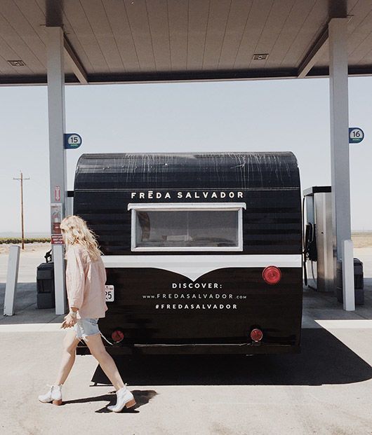 a woman walking past a black and white camper parked at a gas station in the desert