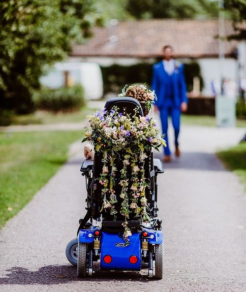 a person in a blue suit walking down a path with a flower arrangement on the back of a motorized scooter