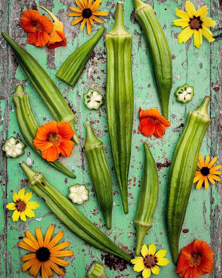 an arrangement of flowers and vegetables on a green surface with peeling paint, including zucchini