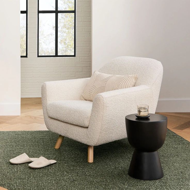 a white chair sitting on top of a green rug next to a black end table