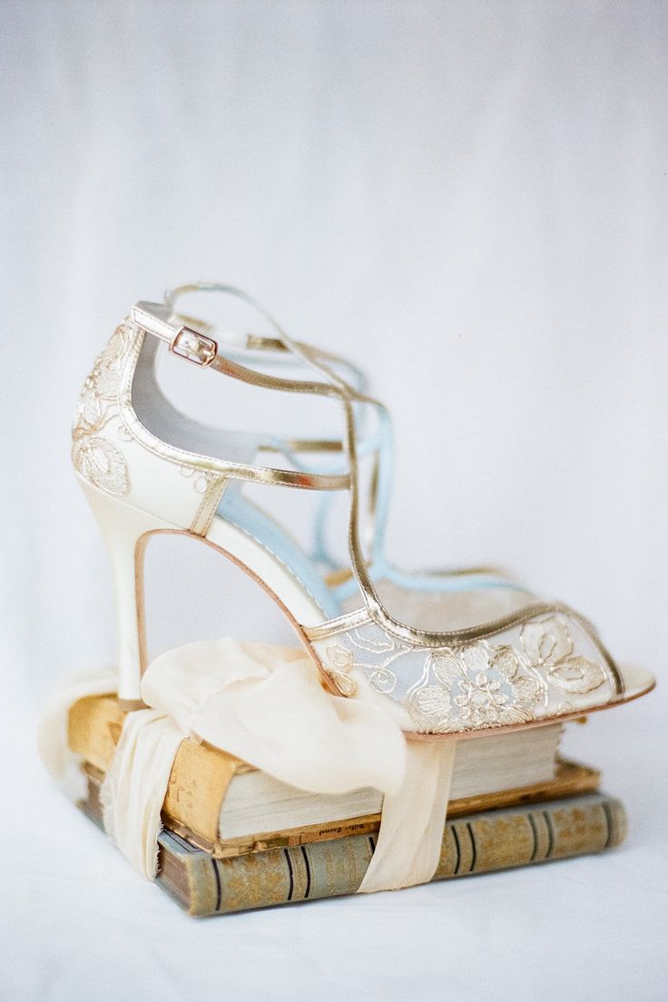 a pair of wedding shoes sitting on top of a stack of books in front of a white background