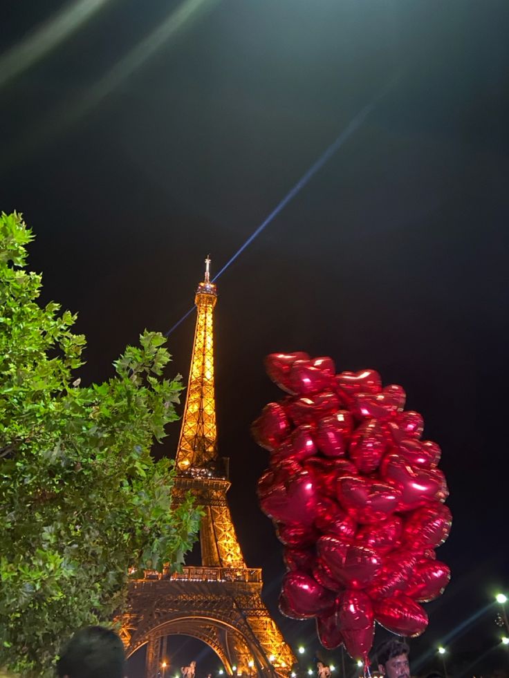 the eiffel tower is lit up with red balloons