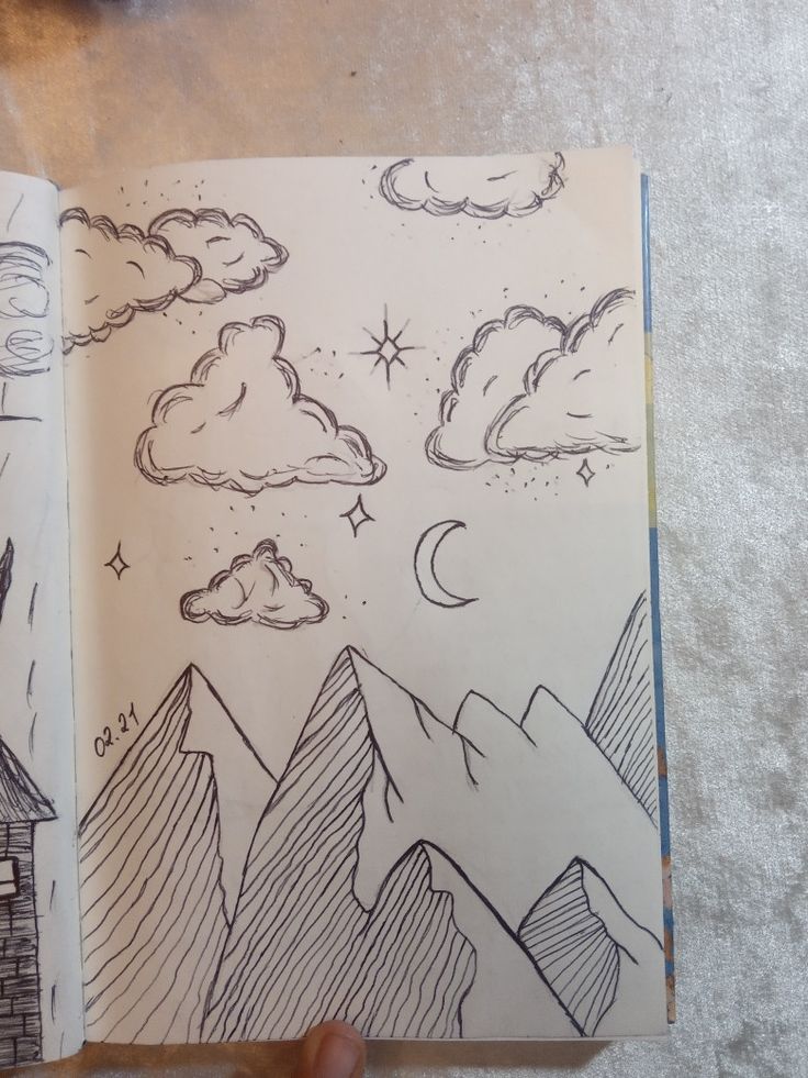 a hand holding an open sketch book with mountains and stars in the sky on it