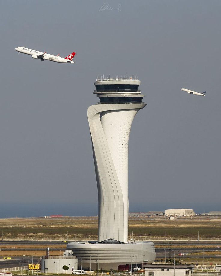 two airplanes flying over an airport with a control tower in the foreground and another plane on the far side