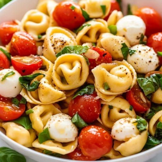 pasta salad with tomatoes, mozzarella and spinach in a white bowl on a table