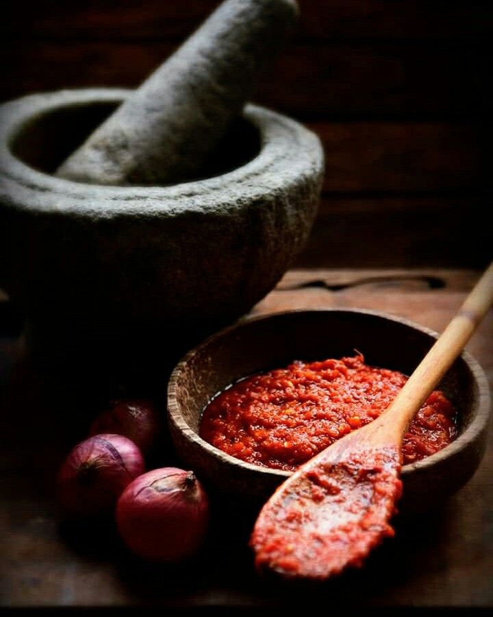 a wooden bowl filled with red sauce next to garlic and an old mortar mortar jar