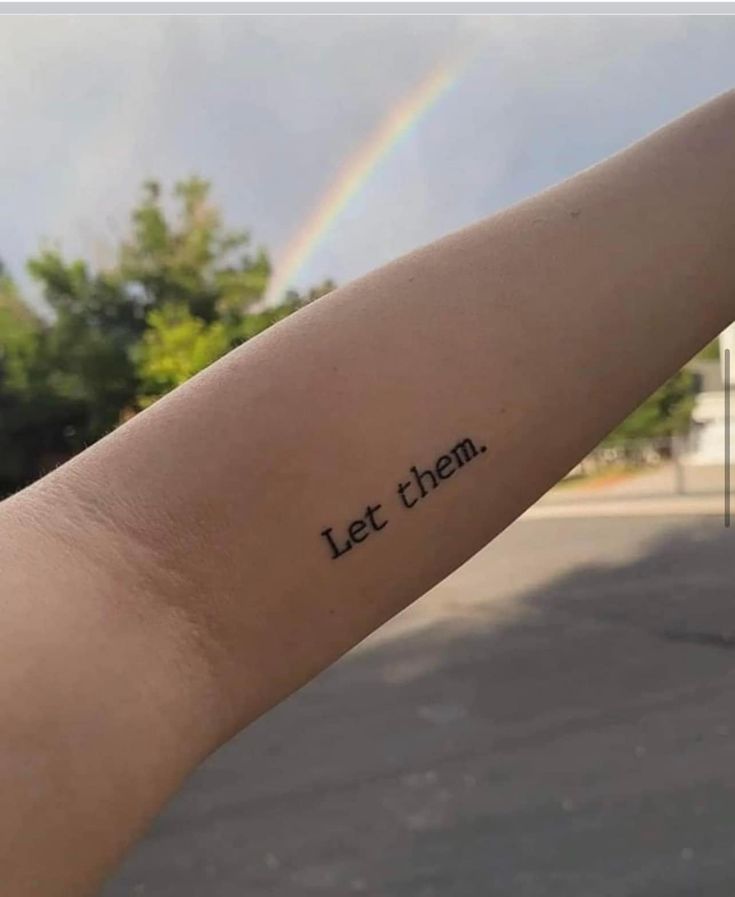 a person's arm with the words let them on it and a rainbow in the background