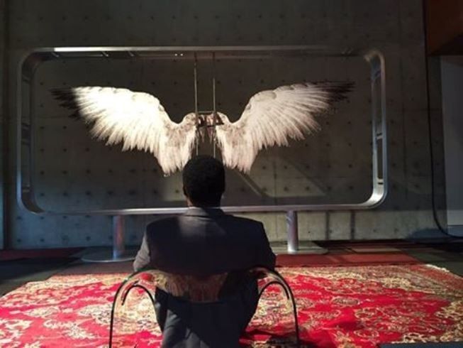 a man sitting on top of a red rug in front of an angel wing sculpture