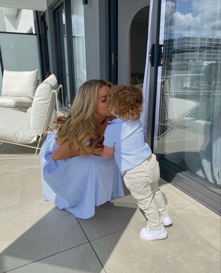 a woman kissing a little boy on the cheek outside in front of a patio area