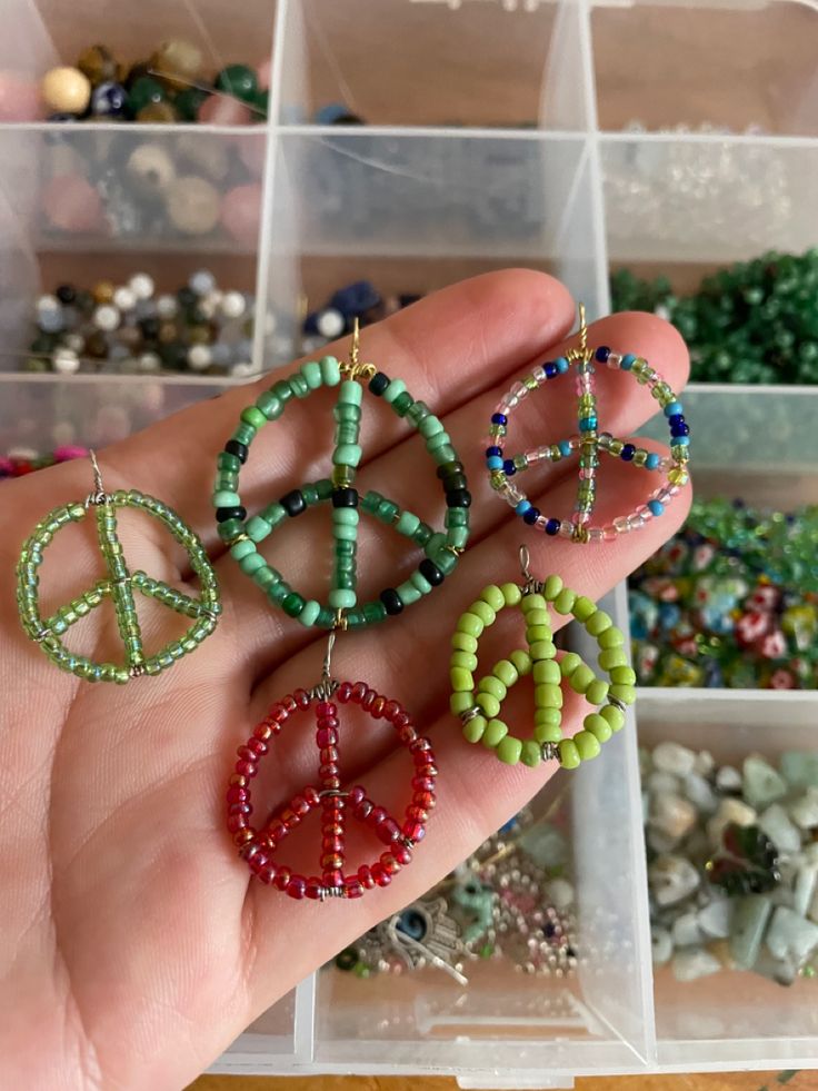 a hand holding three pairs of beaded peace signs and beads in plastic storage bins