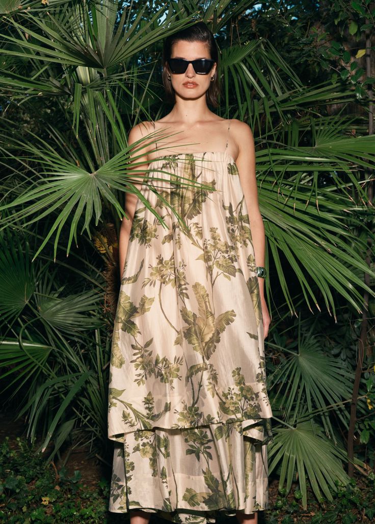 a woman standing in front of palm trees wearing sunglasses and a dress with flowers on it