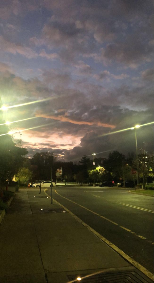 an empty street at night with lights shining on the buildings and clouds in the sky