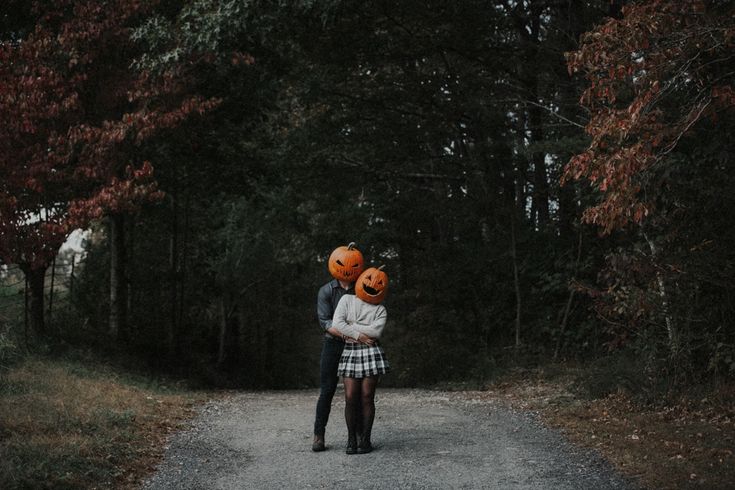 a man and woman standing in the middle of a road with pumpkins on their heads