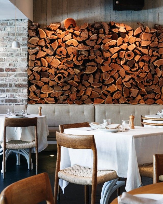 a restaurant with tables and chairs covered in white tablecloths next to a large pile of wood