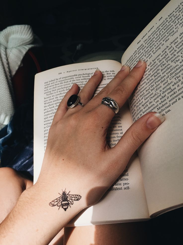 a woman's hand with a bee tattoo on her left wrist reading a book