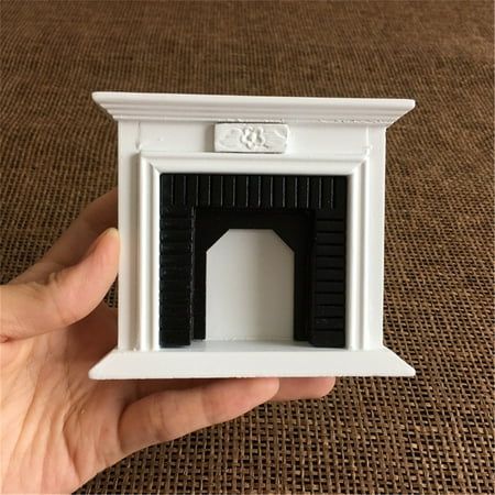 a hand is holding a miniature white and black fireplace mantel with the door open