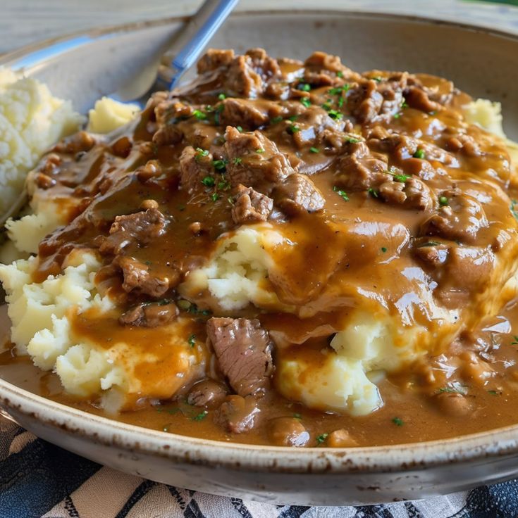 a bowl filled with meat and gravy on top of mashed potatoes