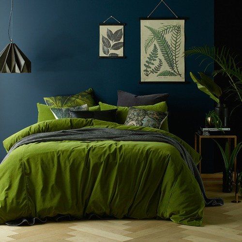 a bed with green sheets and pillows in a blue room next to potted plants