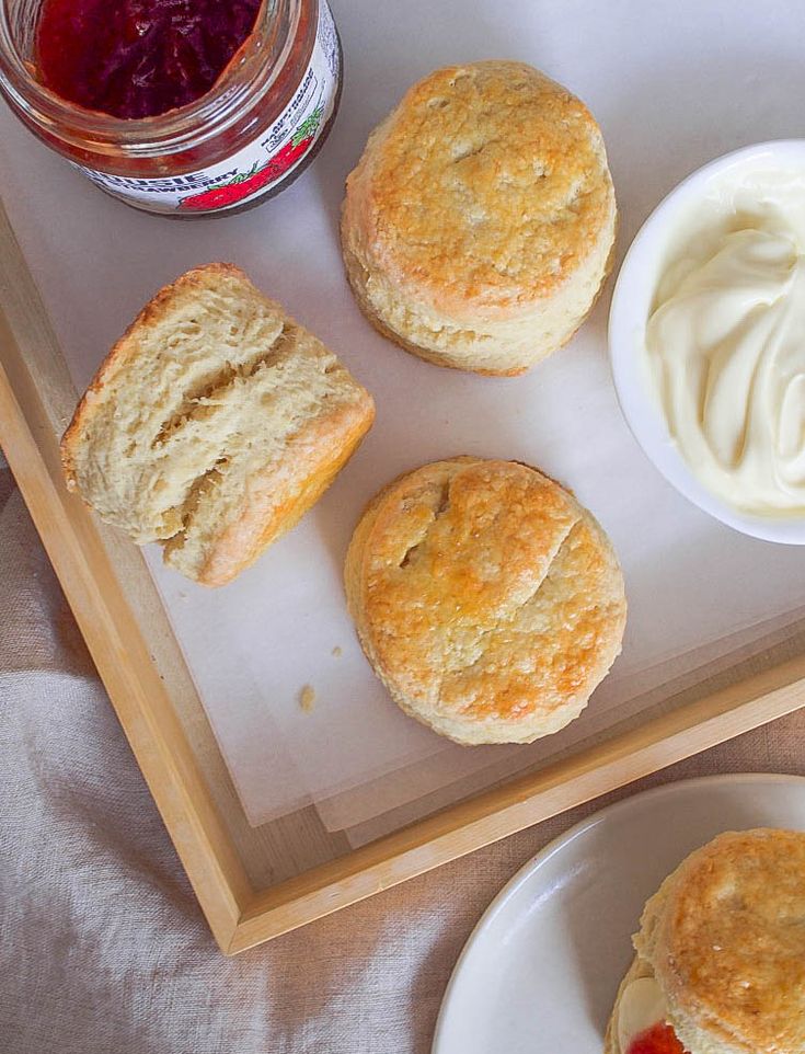 biscuits and cream are on a tray next to a jar of jelly