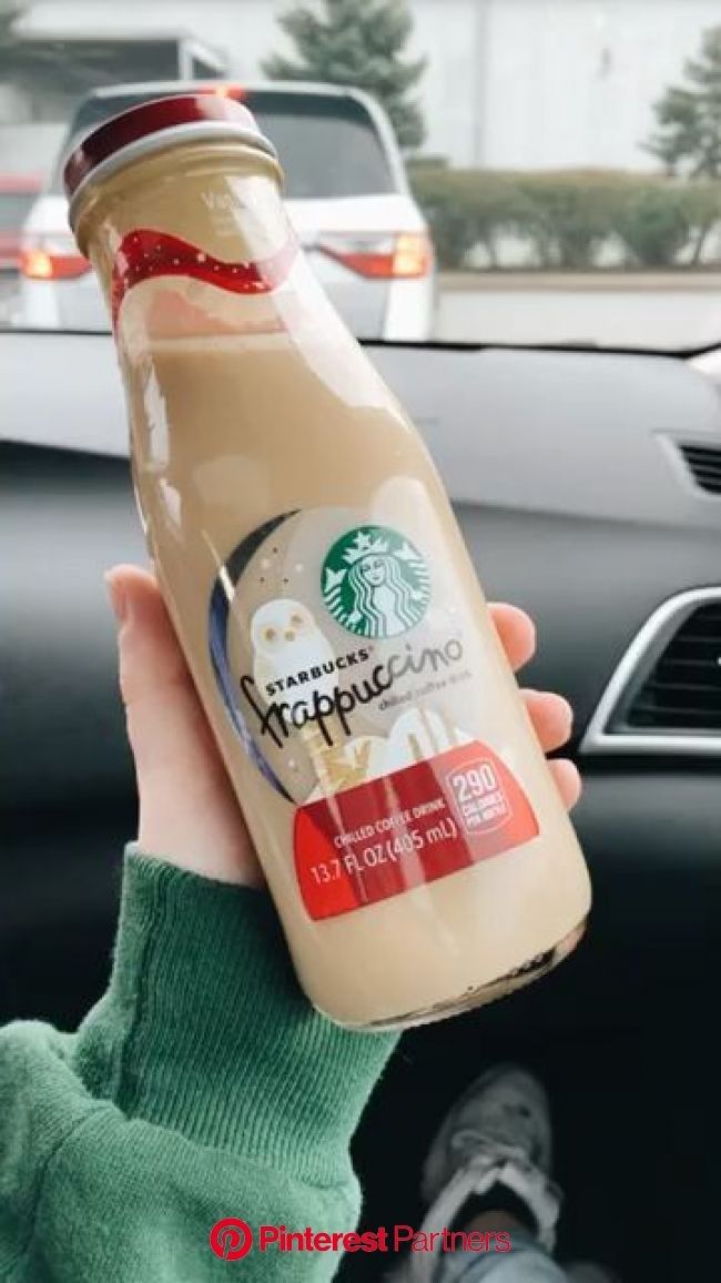 a person holding up a bottle of starbucks coffee in front of a car window with other cars behind them