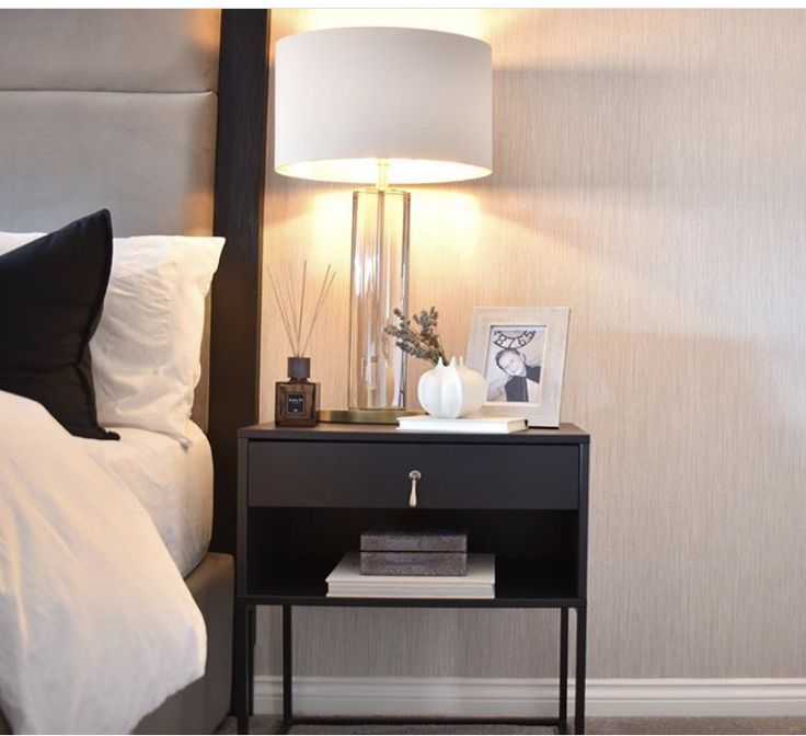 a nightstand with a lamp on top of it next to a bed