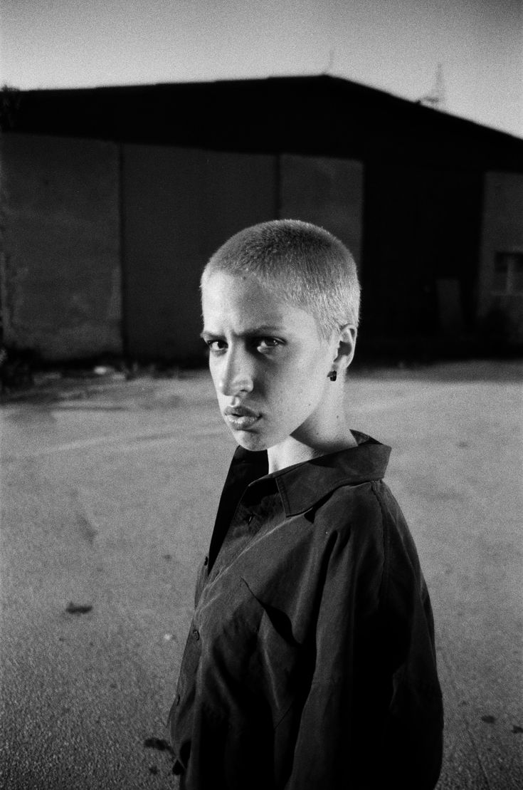 black and white photograph of a young man with shaved hair standing in front of a building