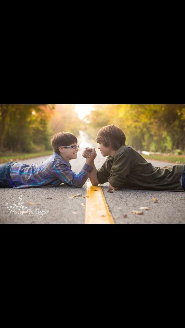 two young boys laying on the road with their hands together