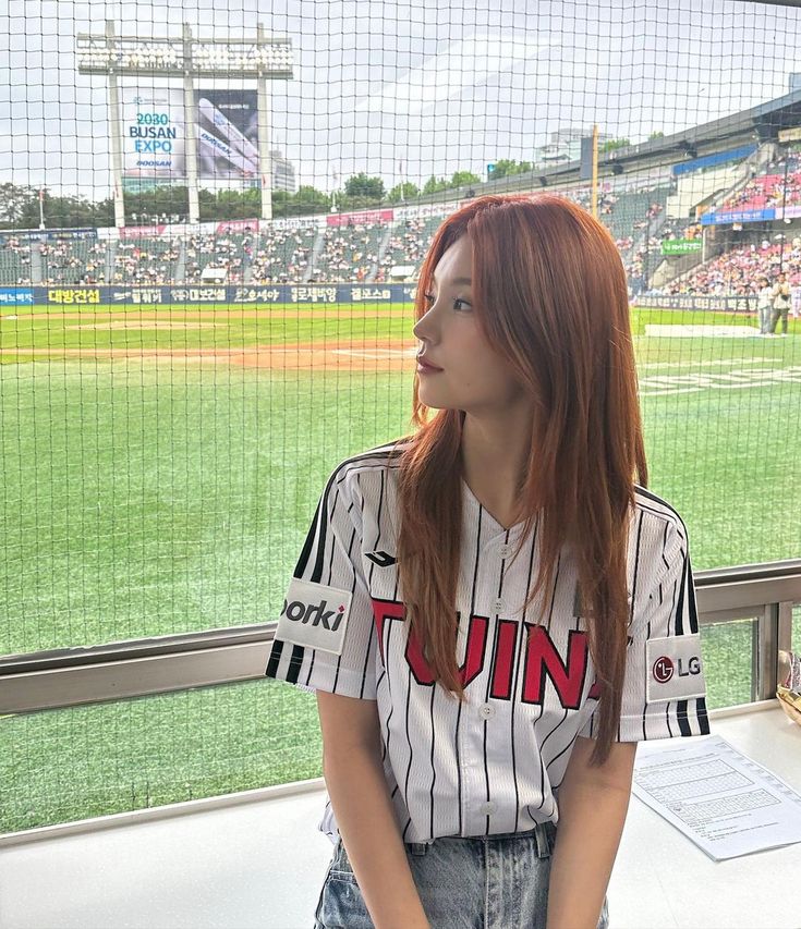 a young woman sitting on top of a bench in front of a baseball field at a stadium