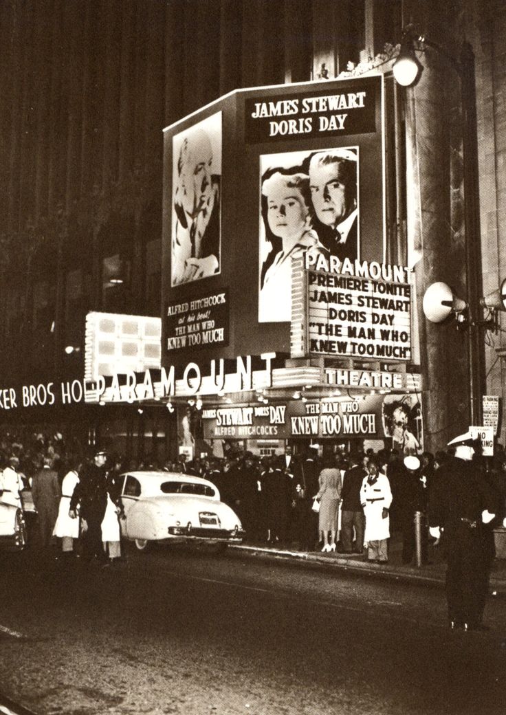 an old black and white photo of people standing in front of a movie theater at night