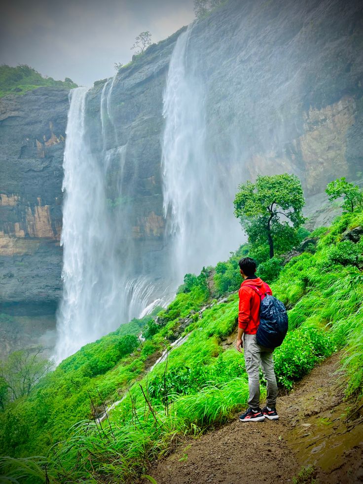 a man with a backpack standing in front of a waterfall