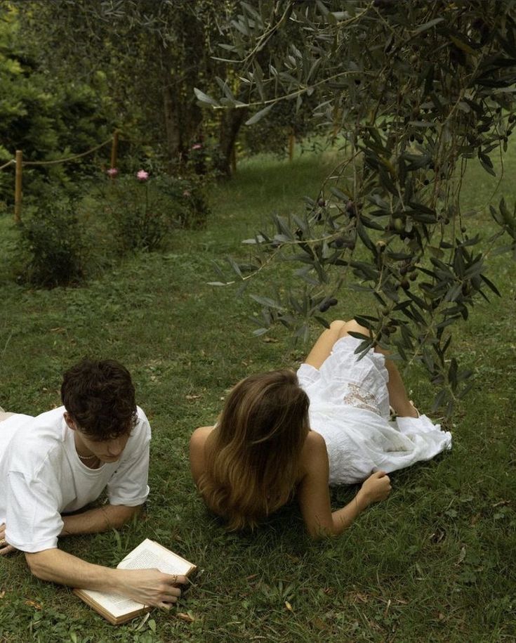 a man and woman laying on the grass reading