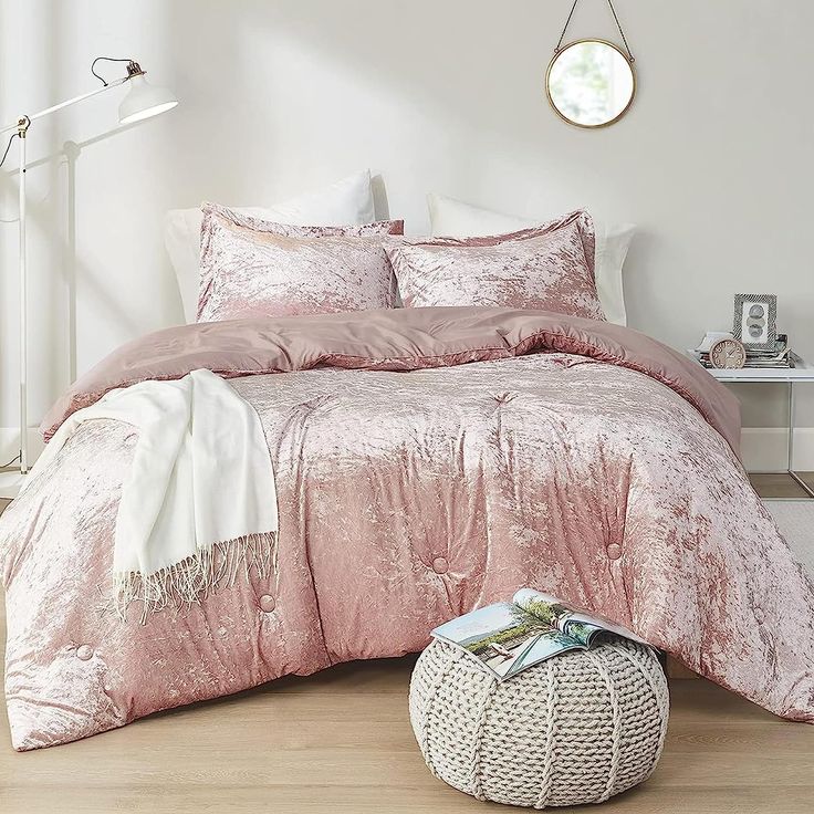 a bed with pink comforter and pillows in a white room next to a chair