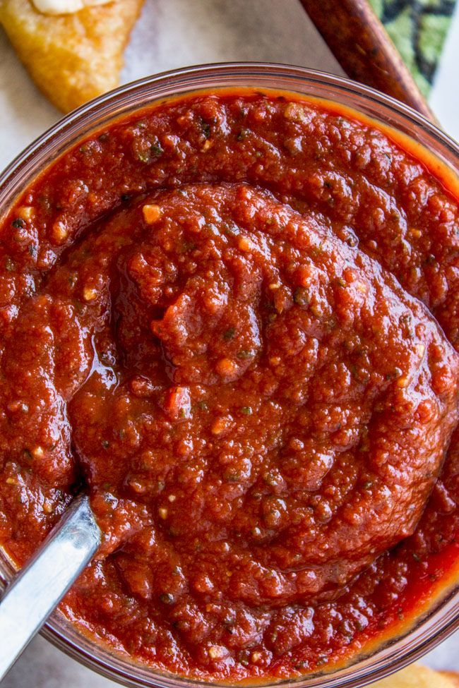 a glass bowl filled with marinara sauce next to breadsticks on a table