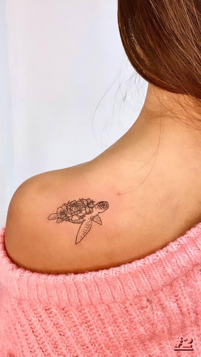 a woman with a turtle tattoo on her back shoulder and behind her neck is a pink sweater