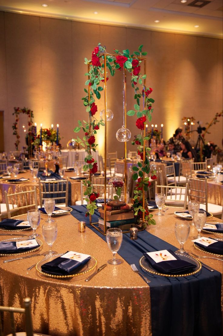 the tables are set up with gold linens and blue tablecloths, along with rose - adorned centerpieces