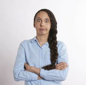 a woman with her arms crossed and eyes wide open, wearing a light blue shirt