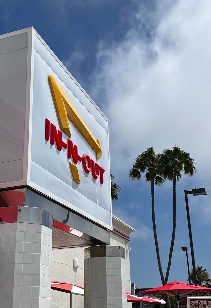 an in - n - out sign on the side of a building with palm trees behind it