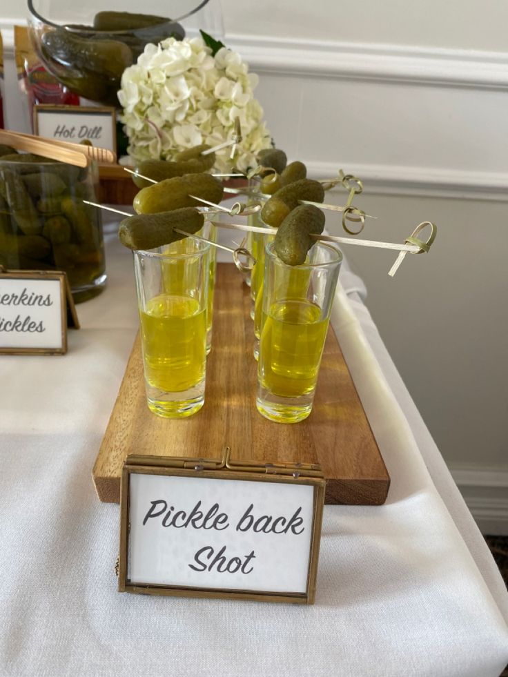 pickle back shot glasses with pickles in them sitting on a wooden tray next to white flowers