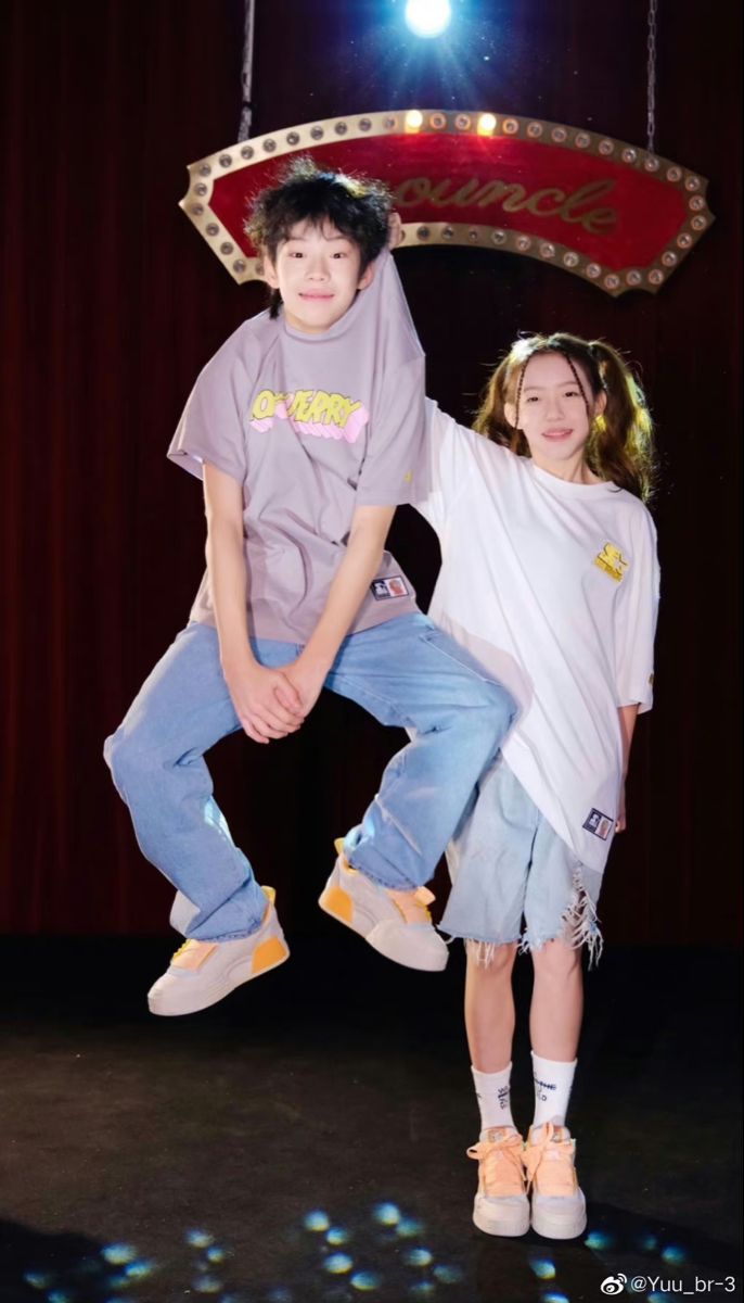 two children posing for a photo in front of a stage backdrop with a sign behind them